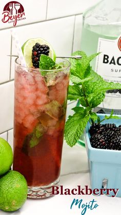 a blackberry mojito with limes and blackberries on the side next to a bottle of booze