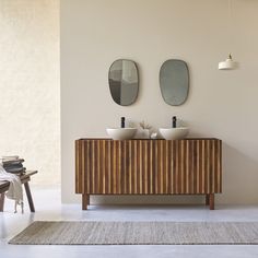 two mirrors on the wall above a wooden cabinet in a room with white walls and rugs