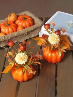 three small pumpkins are sitting on a table with flowers and leaves in the center