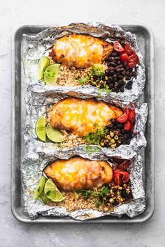 three chicken enchiladas on tin foil with tomatoes, black beans and avocado