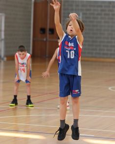 two young boys playing basketball on a court with one reaching up to the ball in the air