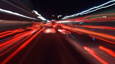 blurry photograph of city street at night with red and white light streaks on the road