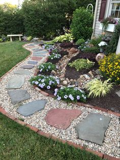 a garden with rocks and flowers in the front yard, along side a house on a sunny day