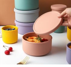 a person holding a container with food in it on a table next to cups and forks