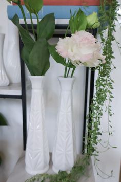 three white vases with flowers and greenery in them sitting on a shelf next to a painting