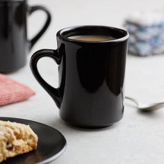 two black coffee mugs sitting next to each other on top of a table with cookies