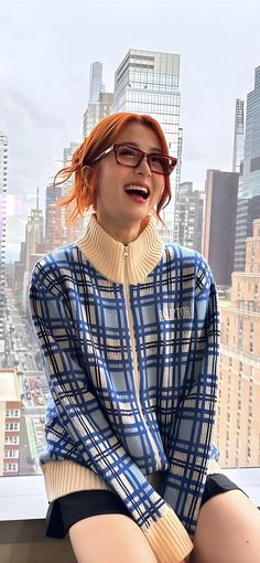 a woman sitting on top of a window sill in front of a cityscape