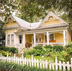 a yellow house with a white picket fence in front of it and lots of greenery