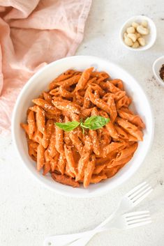 a white bowl filled with pasta and sauce next to two small bowls of nuts on the side