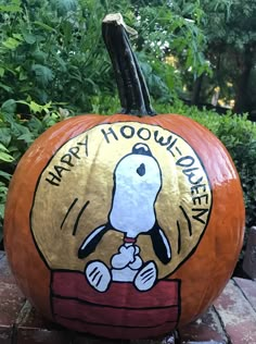 a pumpkin with a snoopy dog on it sitting in front of some bushes and trees