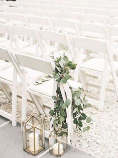 two white chairs with greenery tied to them and candles on the ground in front of them