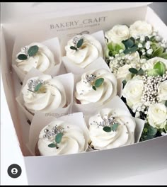 a box filled with cupcakes covered in white frosting and surrounded by greenery