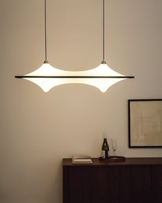 three lights hanging from the ceiling above a table with a wine glass and bottle on it