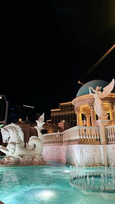 a fountain in the middle of a pool with statues on it and buildings in the background