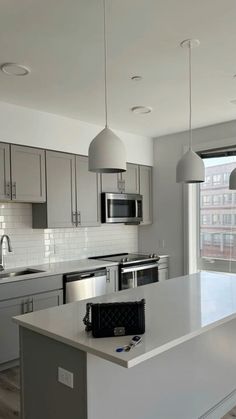 an empty kitchen with stainless steel appliances and white counter tops in front of a large window