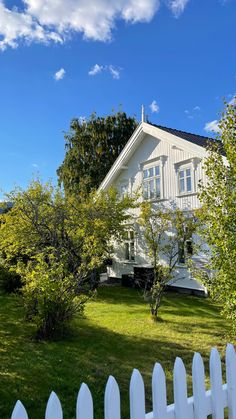 a white picket fence in front of a house with trees and grass on the lawn