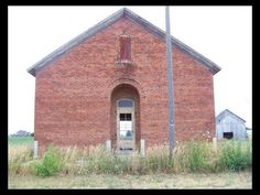 an old red brick building with a door and window in the middle of it's front yard