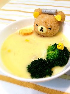 a bowl with broccoli, cheese and a teddy bear in it's head