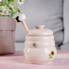 a ceramic tea pot with a bee on it and a flower vase in the background