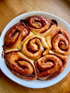 a white plate topped with cinnamon rolls on top of a wooden table