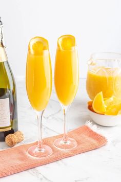 two champagne flutes are sitting on a towel next to a bottle of wine and a bowl of oranges