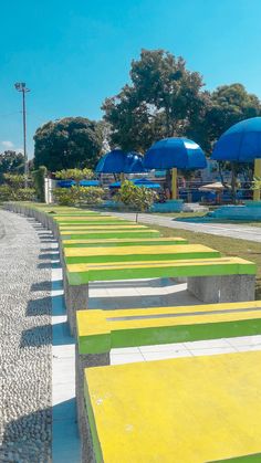 the benches are painted bright yellow, green and blue with umbrellas in the background