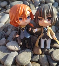 two anime figurines sitting on top of rocks next to each other with their hands together