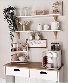 a coffee bar with cups and mugs on the shelves above it is decorated with greenery