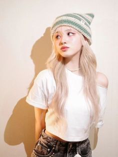 a woman with long blonde hair wearing a white shirt and green knitted beanie