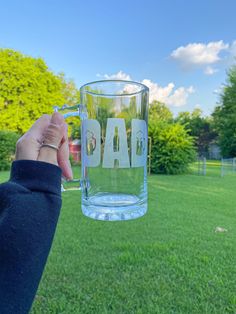 a person holding up a glass with the word dad on it in front of a grassy field