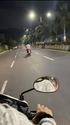 a person riding a motorcycle down the middle of a street at night with lights on