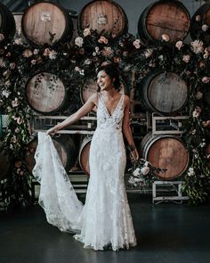 a woman standing in front of wine barrels holding a wedding dress and smiling at the camera