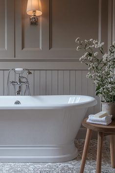 a white bath tub sitting in a bathroom next to a table with flowers on it