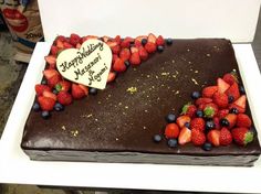 a heart shaped chocolate cake with strawberries and blueberries on the side, sitting on a white plate