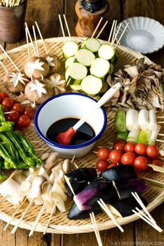 an assortment of vegetables on skewers in a bowl with dipping sauce and toothpicks