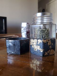 a glass jar filled with dirt sitting on top of a wooden table next to a black container