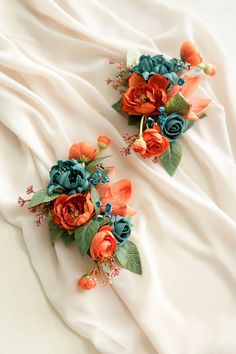 two bridal bouquets with orange and teal flowers on white satin fabric background