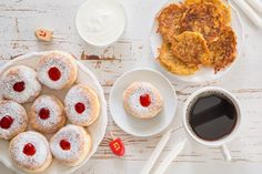 a table topped with pastries and coffee next to other foods on white plates covered in powdered sugar