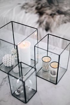 three glass cubes with candles and balls in them on a marble table top next to a furry animal