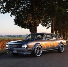 an old car is parked on the side of the road in front of some trees