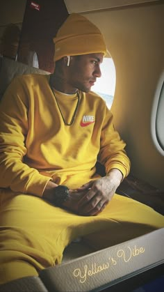 a man sitting on an airplane seat wearing a yellow nike sweater and beanie hat