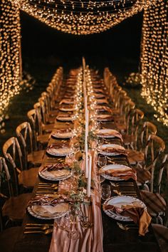 a long table is set with plates and place settings for an outdoor dinner party at night