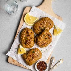 some food is sitting on a cutting board with lemons and seasoning next to it