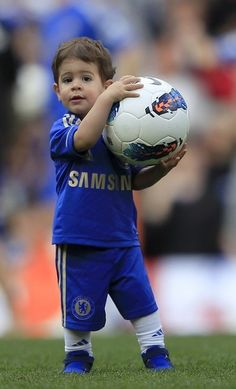 a young boy holding a soccer ball on top of a field