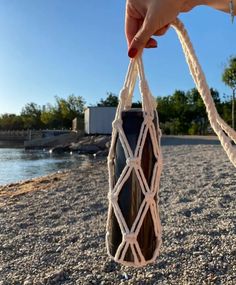 a hand holding a rope wrapped bottle on the beach