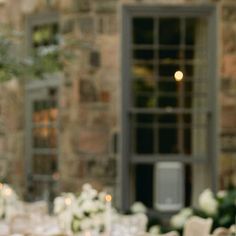 the table is set with white flowers and candles for an elegant wedding reception in front of a stone building