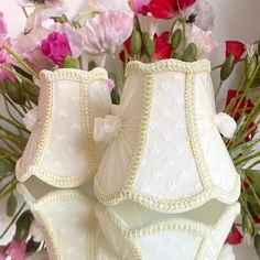 two white lampshades sitting on top of each other in front of pink flowers