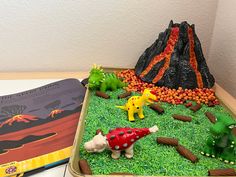 there is a dinosaur cake in the shape of a volcano and other toys on the table