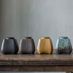 four different colored vases sitting on top of a wooden table next to each other