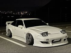 a white sports car parked in a parking lot at night with city lights in the background